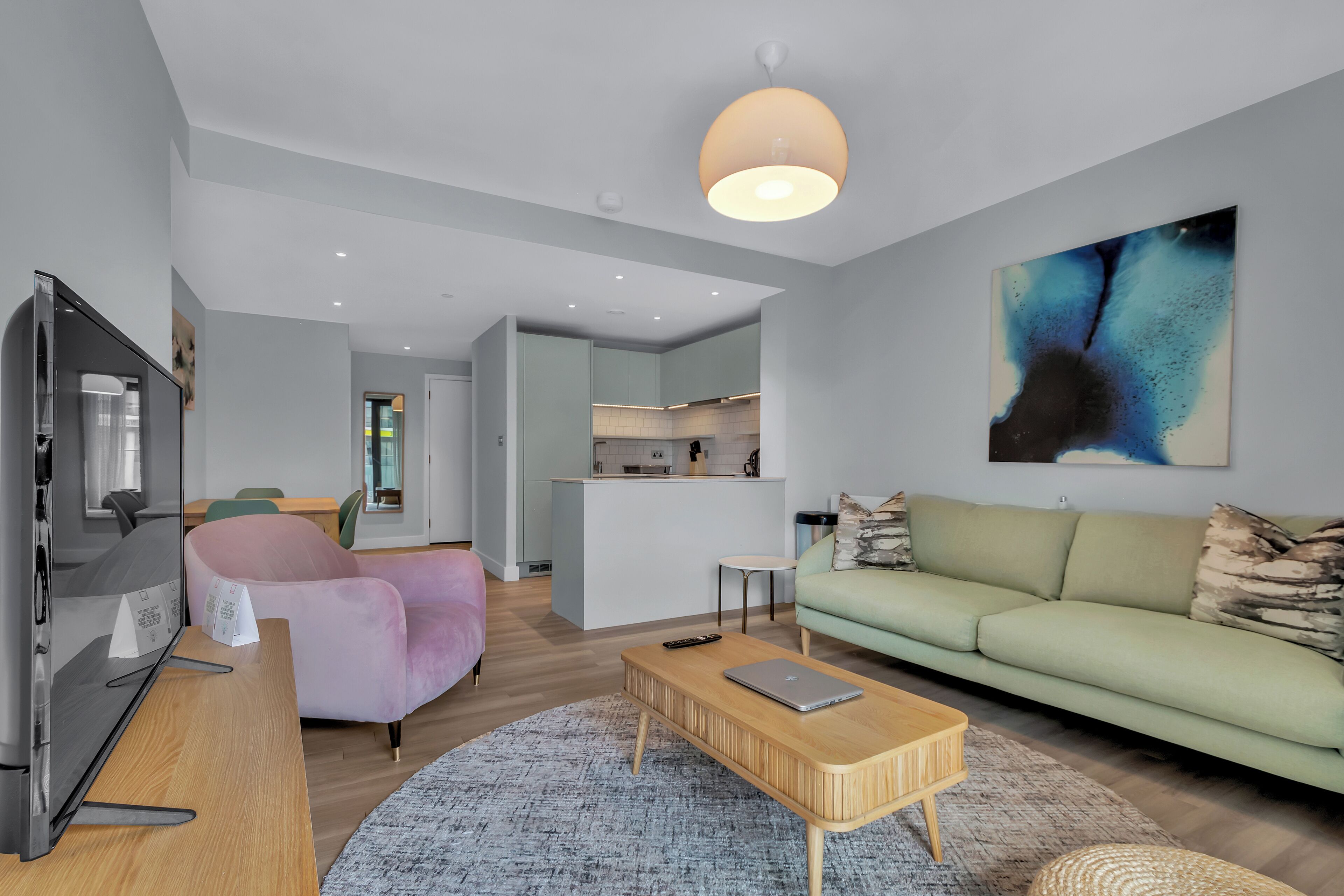 A modern living room with a sofa, a coffee table, and a TV. There is a kitchen area in the background.