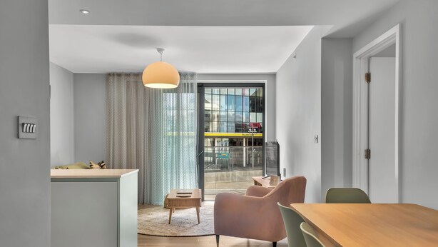 Una sala de estar moderna con una mesa de comedor de madera, un sofá rosa y un ventanal con vista a la ciudad.