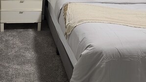 Een slaapkamer met een bed, nachtkastje, lamp en een raam met zonwering.