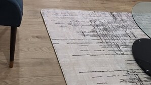 Een moderne woonkamer met een grijze bank, een tapijt met een patroon en een eethoek met een zwarte tafel en stoelen.