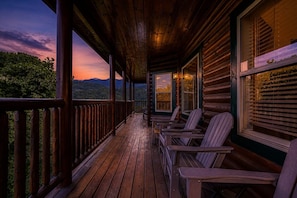 A wooden porch with Adirondack chairs, a view of mountains, and a wooden cabin structure.