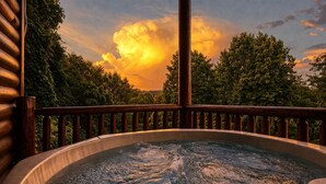 A hot tub with a wooden deck and railing, surrounded by trees and a sunset sky. - Greystone- pet friendly, walk to Gatlinburg! (Gatlinburg)