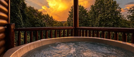 Un jacuzzi con cubierta de madera y barandilla, rodeado de árboles y un cielo al atardecer.
