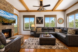 A living room with a stone fireplace, leather sofas, a large flat-screen TV, and a ceiling fan.