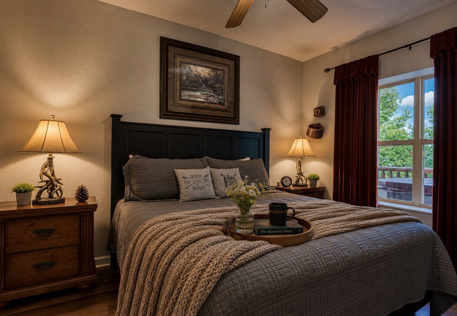 A bedroom with a bed, two bedside tables, a nightstand, a ceiling fan, a window with curtains, and a framed picture on the wall.