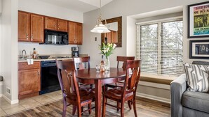 Une cuisine moderne avec des meubles en bois, une table à manger avec des chaises et une fenêtre avec des stores.