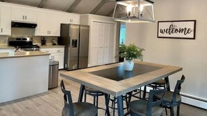 A modern kitchen with white cabinets, a stainless steel refrigerator, a wooden island with a bench, and a hanging light fixture.