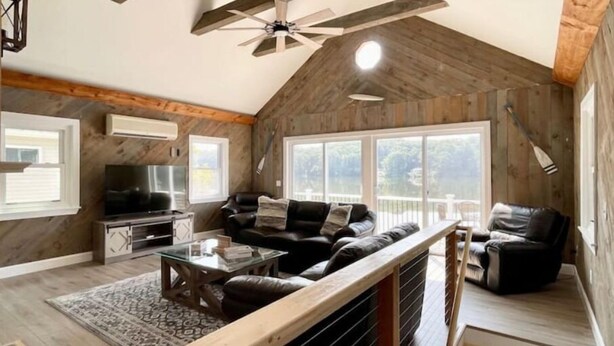 A spacious loft with a high ceiling, exposed wooden beams, a large window, and a cozy seating area with a TV and coffee table.