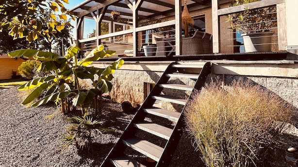 Un espacio al aire libre techado con una escalera de madera que da a una zona de estar con mobiliario de mimbre.