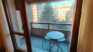 Un balcón con mesa y sillas, vistas a edificios y un árbol.