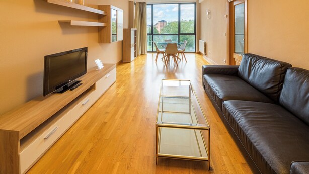 A modern living room with a flat-screen TV, a glass coffee table, a leather sofa, and a dining area with a table and chairs.