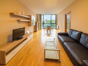 A modern living room with a flat-screen TV, a glass coffee table, a leather sofa, and a dining area with a table and chairs. - Estupendo Apartamento con Vistas a Yamaguchi (Pamplona)