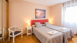 A hotel room with two beds, a chair, a nightstand, and a painting on the wall.