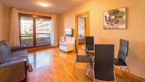 A modern living room with a sofa, a dining table with chairs, a TV, and a balcony with a view of buildings. - Apartamento Ideal Para dos en Pamplona (Pamplona)