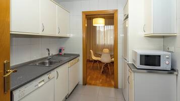 Una cocina compacta con armarios blancos, lavavajillas integrado, microondas y comedor con mesa y sillas.