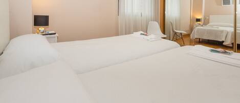 A hotel room with two beds, a flat-screen TV, a bedside table with a lamp, and a chair.