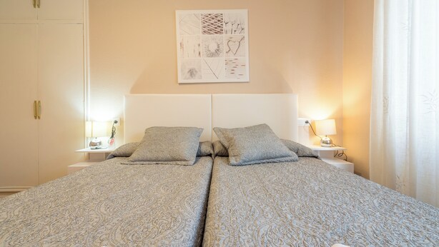Ein Doppelbett mit gemusterten Betttextilien, Nachttische mit Lampen, ein Kleiderschrank und ein Wandbild.