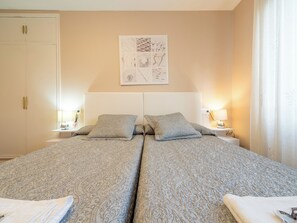Een tweepersoonsbed met beddengoed met patroon, nachtkastjes met lampen, een kledingkast en een kunstwerk aan de muur.