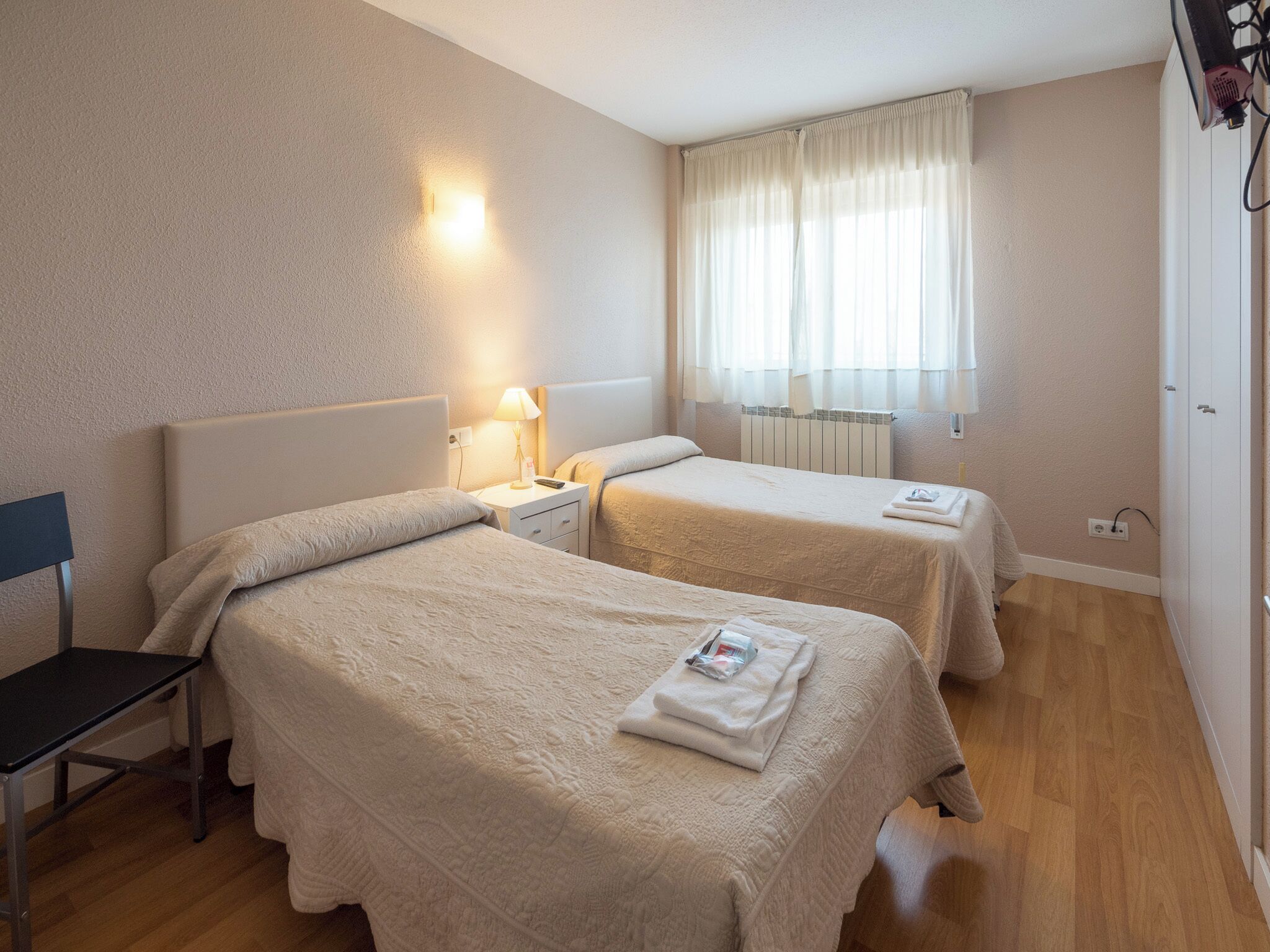 Ein Hotelzimmer mit zwei Betten, einem Schreibtisch und einem fenster mit Vorhängen.