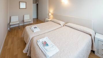 Een hotelkamer met twee bedden, een nachtkastje met een lamp, een stoel en een ingelijste foto aan de muur.