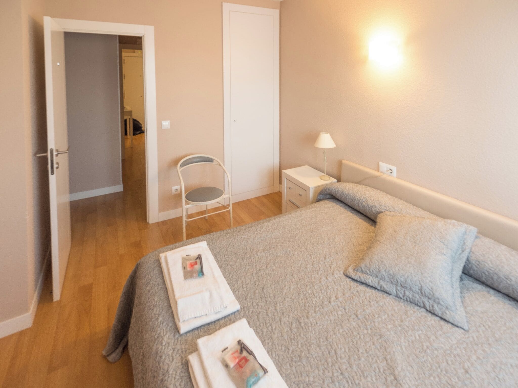 A bedroom with a bed, a nightstand, a chair, and a door leading to another room.