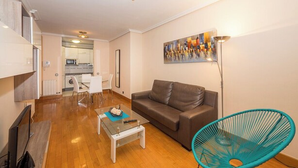 A compact living space with a sofa, a coffee table, a TV, a chair, and a painting on the wall. - Coqueto Apartamento Para 3-4 Personas (Pamplona)
