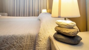 A neatly made bed with a quilted cover, a bedside lamp with a white shade, and a stack of stones on the nightstand. - Coqueto Apartamento Para 3-4 Personas (Pamplona)