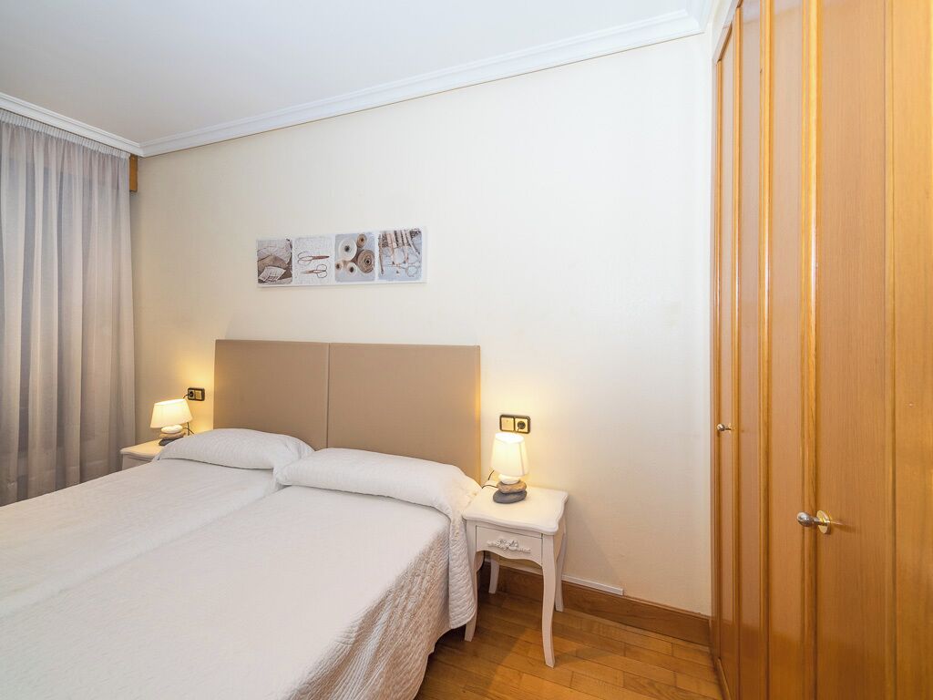 Una habitación de hotel con una cama grande, dos mesitas de noche con lámparas, un armario de madera y obras de arte en la pared.