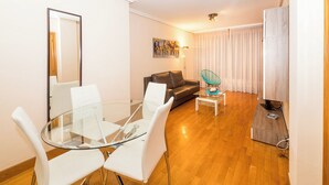 A modern living room with a glass dining table, white chairs, a black leather sofa, and a glass coffee table. - Coqueto Apartamento Para 3-4 Personas (Pamplona)