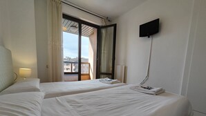 Ein Hotelzimmer mit zwei Betten, einem an der Wand befestigten Fernseher und Blick auf Gebäude durch das Fenster.