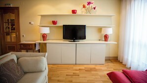 A living room with a TV on a white cabinet, two red lamps, a sofa, and a red chair.