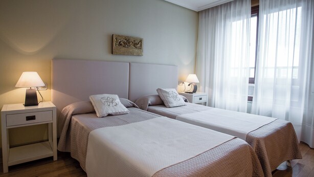 A hotel room with two beds, each with a pillow and a nightstand with a lamp.