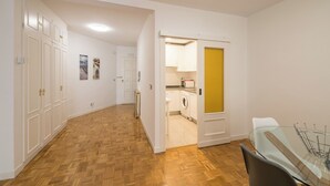 Ein Flur mit Holzboden, einem Glastisch und einer durchgehenden Tür erkennbaren Küchenzeile.