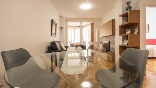 Ein modernes Wohnzimmer mit einem Glastisch, grauen Stühlen, einer Couch und einem Fernseher.