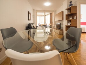 A modern living room with a glass dining table, grey chairs, a sofa, and a TV. - Apartamento a 2 Minutos Caminando de la Clínica Universitaria (Pamplona)