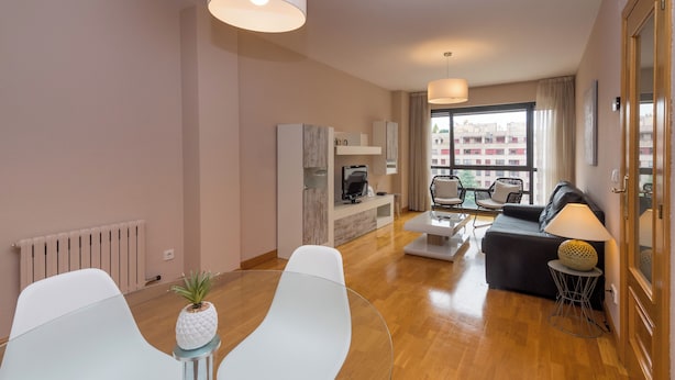 A modern living room with a sofa, two white chairs, a coffee table, and a TV. - Apartamento Zona Clínica Universitaria (Pamplona)