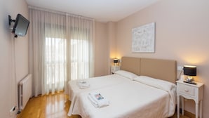 A hotel room with a large bed, two bedside tables, a flat-screen TV mounted on the wall, and a window with sheer curtains. - Apartamento Zona Clínica Universitaria (Pamplona)