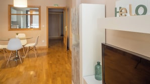 A modern hotel room with a wooden floor, a dining area with a glass table and chairs, and a wall-mounted sign that reads "HELLO". - Apartamento Zona Clínica Universitaria (Pamplona)