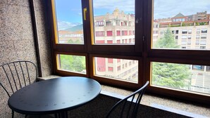 A room with a round table and two chairs, a window with a view of buildings and trees. - Para 4, el Apartamento Idóneo (Pamplona)