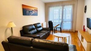 A living room with a black leather sofa, a small round table, a TV on a wooden stand, and a painting on the wall. - Para 4, el Apartamento Idóneo (Pamplona)
