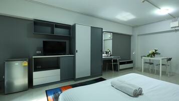 A modern hotel room with a bed, a desk, a television, and a minibar.