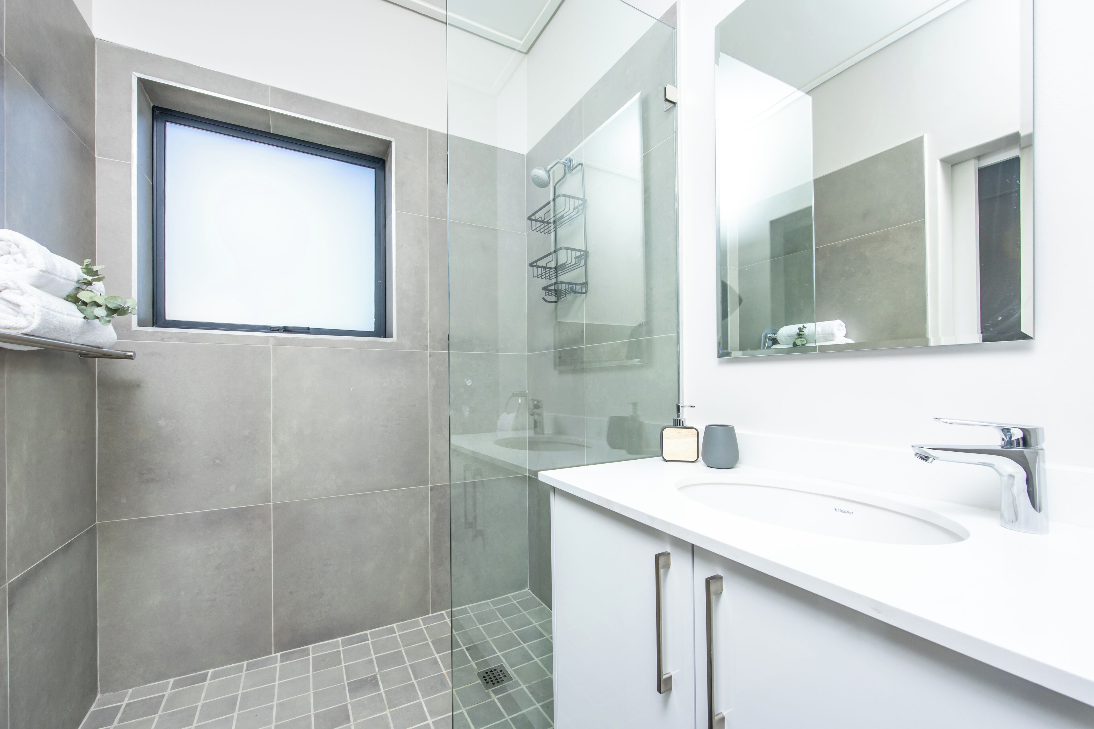 Un baño moderno con un espejo grande, un lavabo blanco y una zona de ducha.