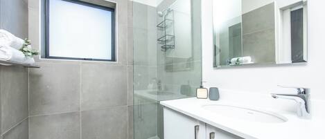 Un baño moderno con un espejo grande, un lavabo blanco y una zona de ducha.