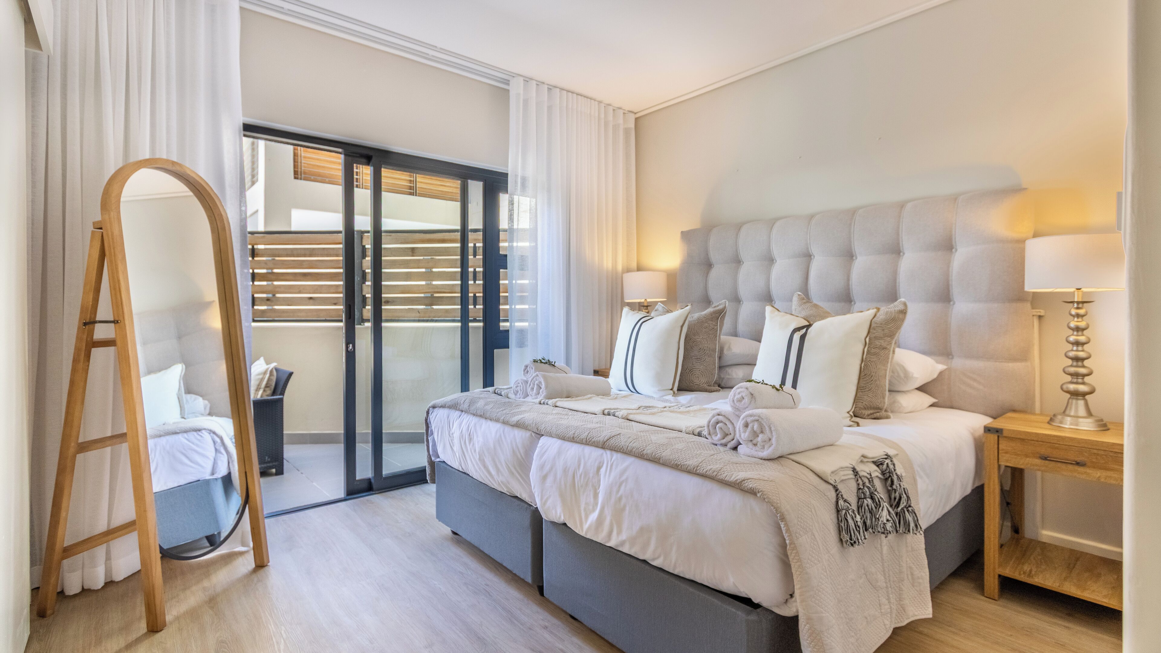 Un dormitorio moderno con una cama grande, una escalera de madera, una mesita de noche y vistas a través de una puerta corrediza de vidrio.