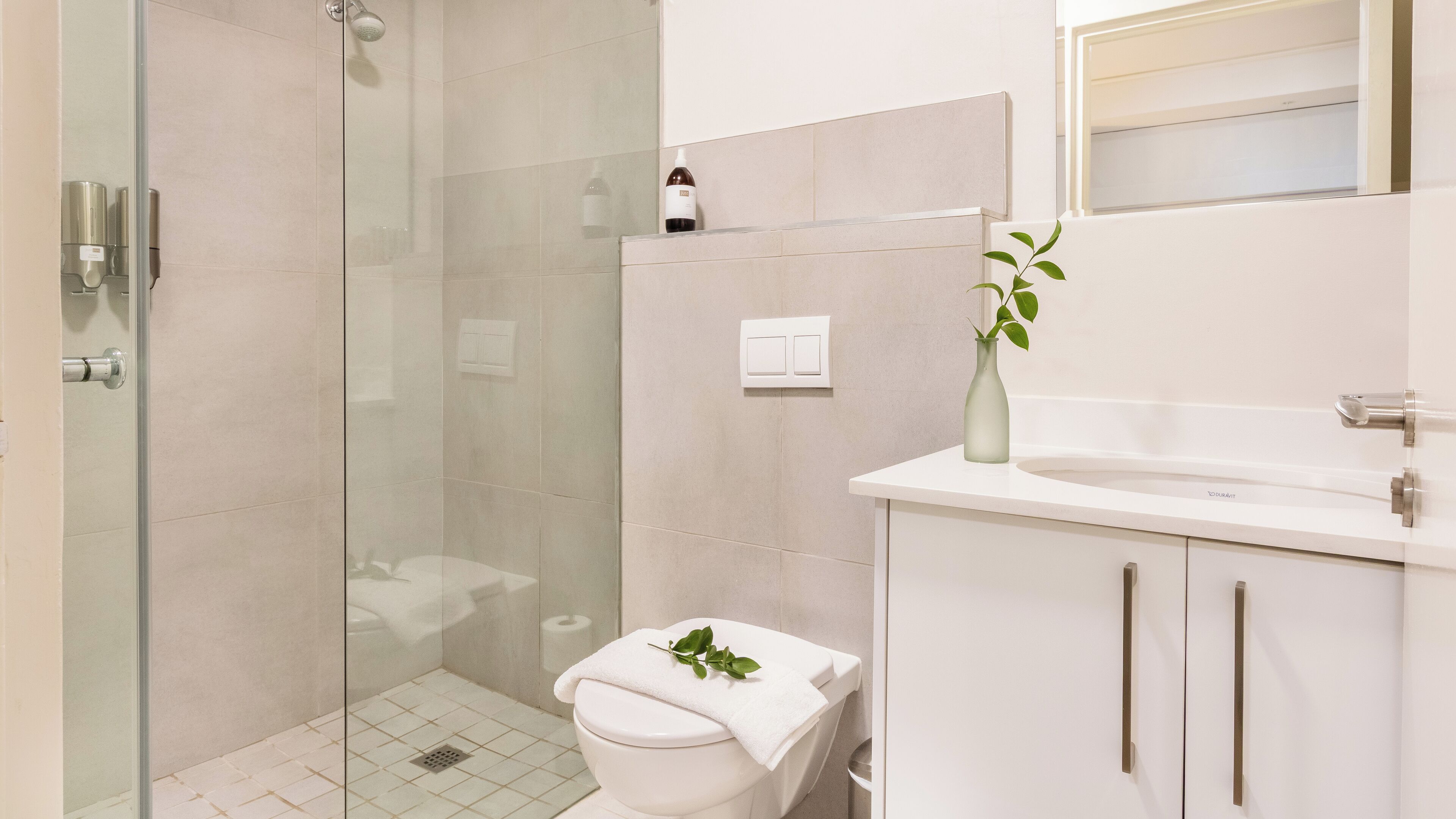 A modern bathroom with a glass shower enclosure, a toilet, and a sink with a vase of greenery.