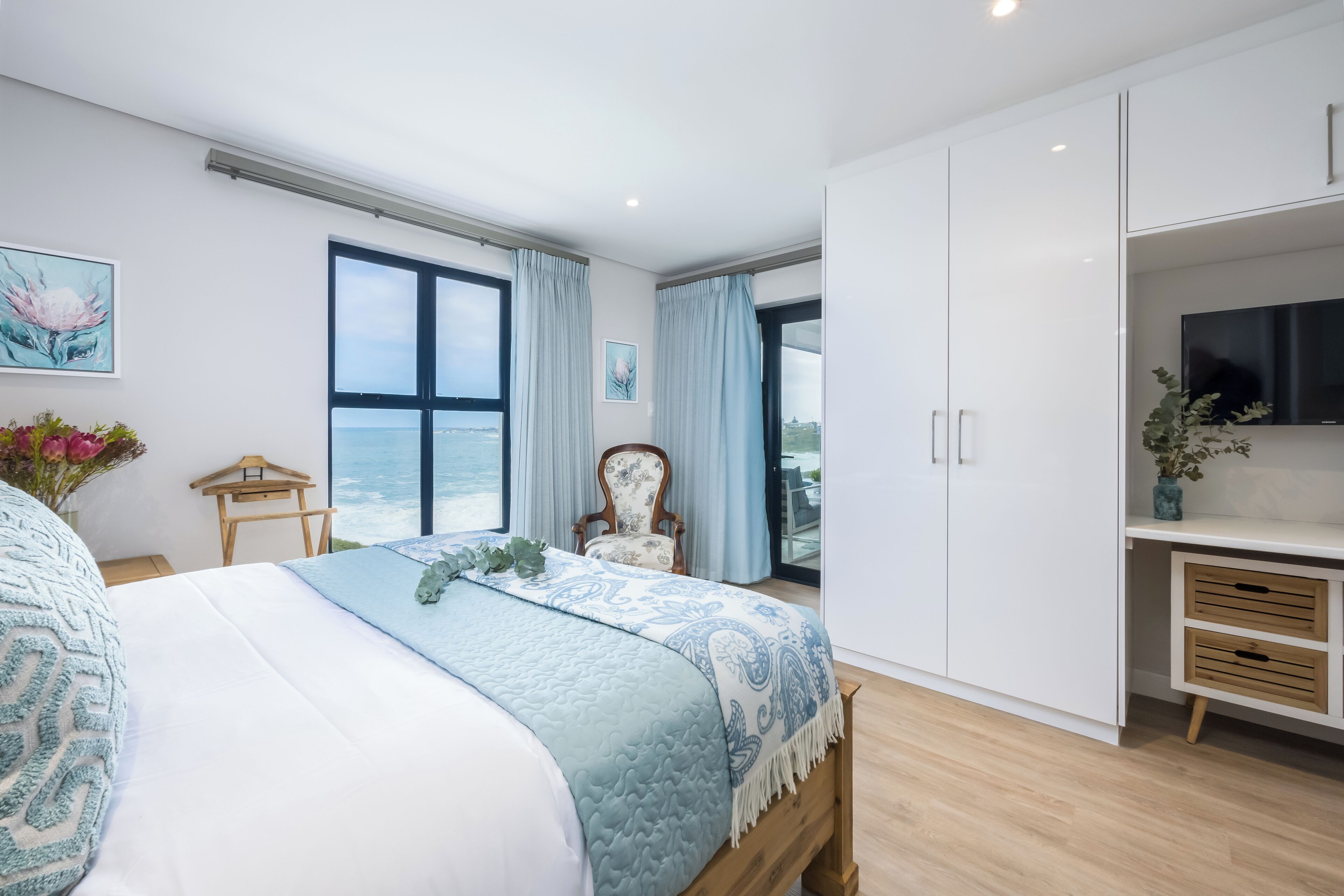 A bedroom with a large bed, a TV, a wardrobe, and a view of the sea.