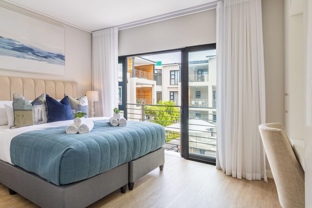 Une chambre d’hôtel moderne avec un grand lit, une vue sur la ville depuis le balcon et un lit parfaitement fait, avec des serviettes soigneusement pliées.