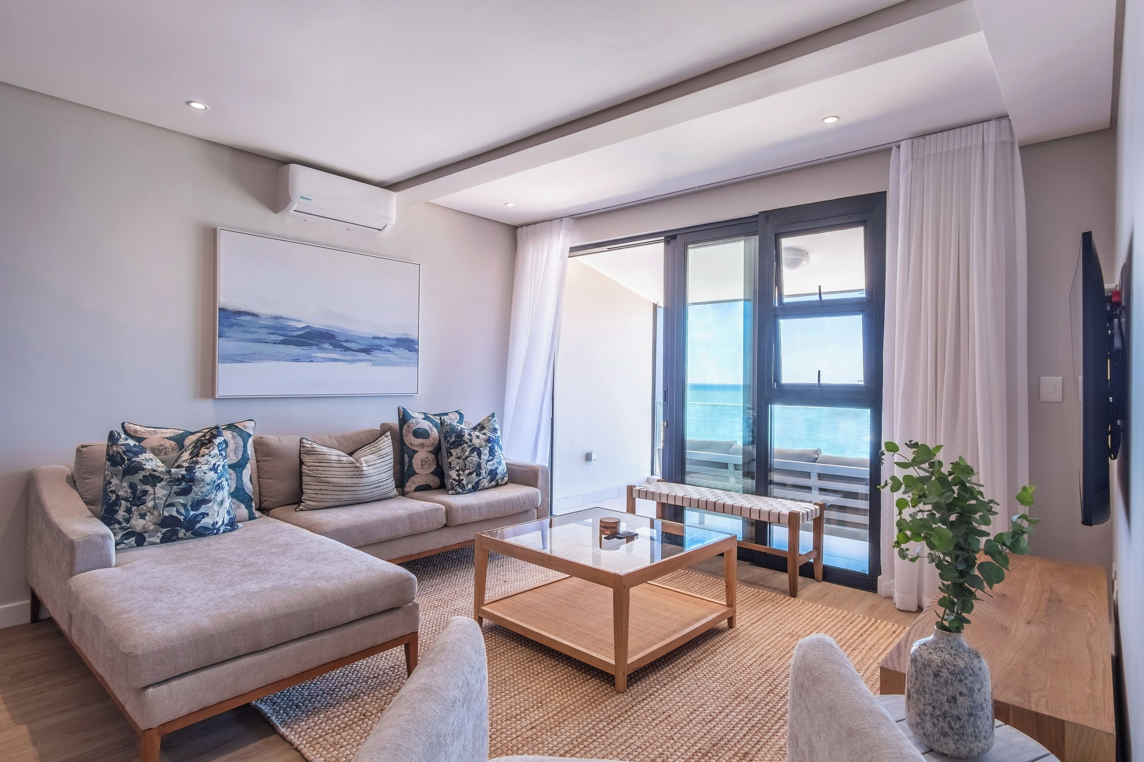 A modern living room with a sofa, coffee table, and a view of the sea through large windows.
