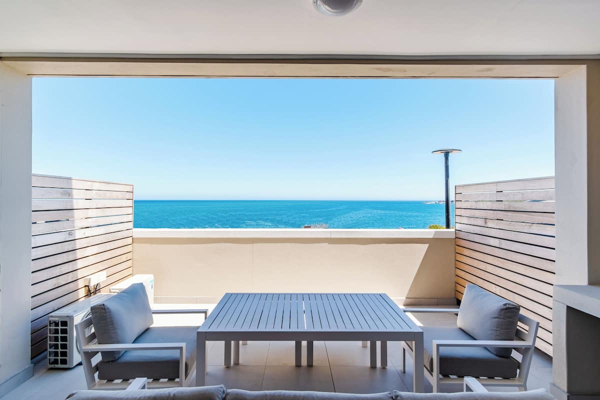 Un balcon avec une table et deux chaises, donnant sur une mer d’un bleu limpide.