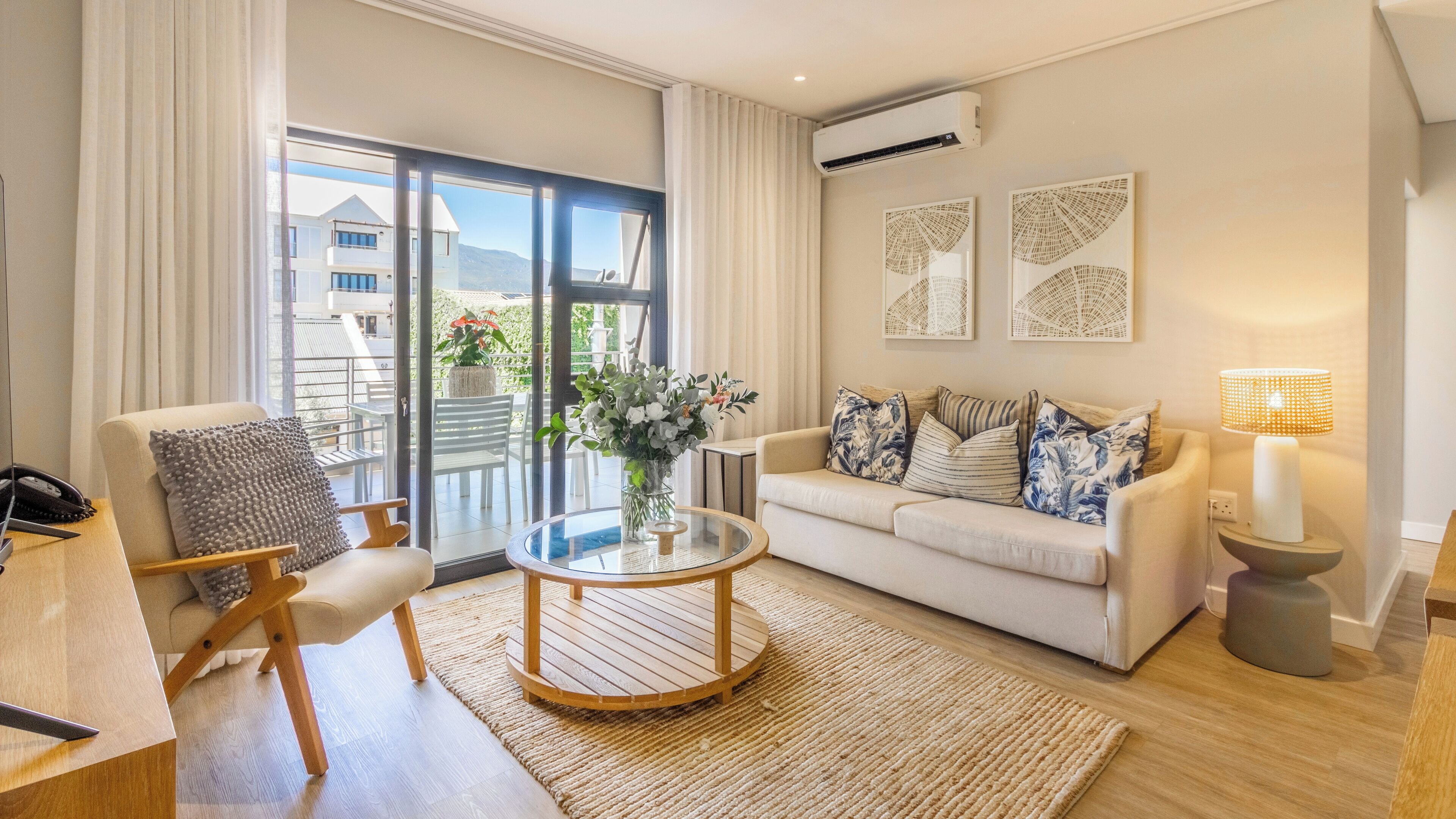 Una sala de estar moderna con sofá, sillón, mesa de centro y vistas al exterior a través de amplios ventanales.